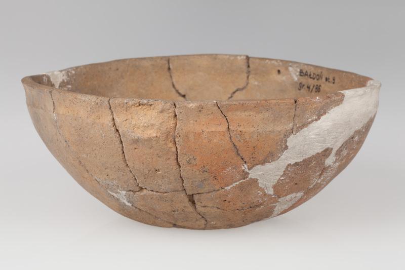 Misa półokrągła ze słabo zaznaczonym dnem, o gładkiej szyjce i szorstkim brzuścu. Ornamentowana dookolnymi pionowymi żłobkami.