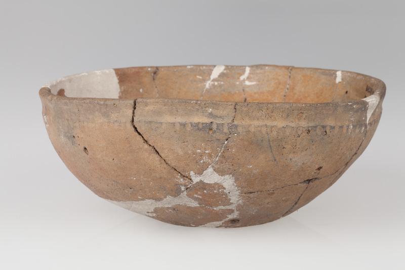 Misa półokrągła ze słabo zaznaczonym dnem, o gładkiej szyjce i szorstkim brzuścu. Ornamentowana dookolnymi pionowymi żłobkami.