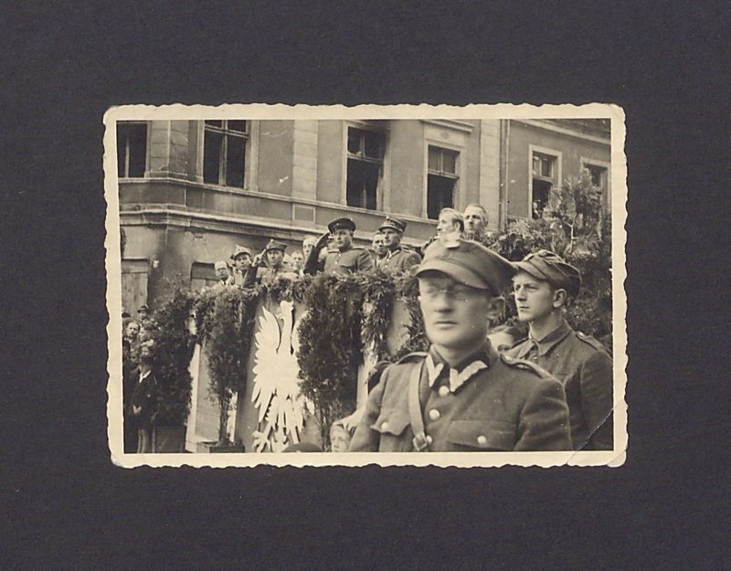 Uroczystości 3-go Maja w Gnieźnie. Uczestnicy pochodu na tle trybuny ustawionej przed budynkiem, na narożniku ulic Chrobrego i Mieszka I 