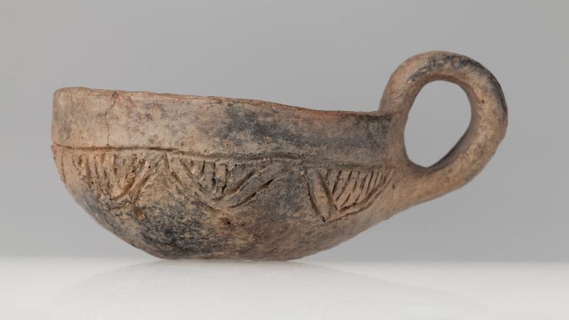 Czerpak półkulisty z wklęsłym dnem, zdobiony dookolnym rytym rowkiem i zwężającymi się trójkątami