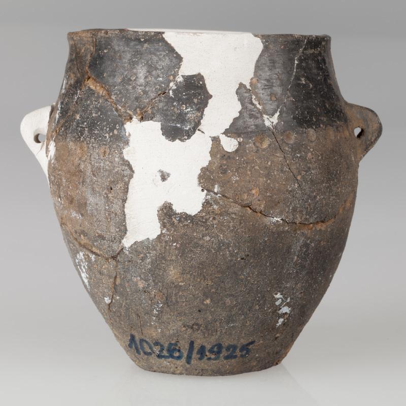 Garnek beczułkowaty zaopatrzony w dwa kolankowate, poziomo przekłute uszka