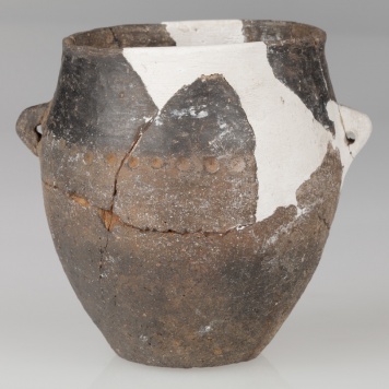 Garnek beczułkowaty zaopatrzony w dwa kolankowate, poziomo przekłute uszka